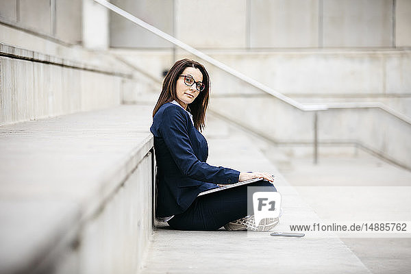 Porträt einer Geschäftsfrau  die mit Laptop im Freien auf einer Treppe sitzt