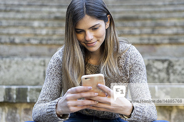 Junge Frau sitzt auf einer Treppe im Freien und benutzt ihr Handy