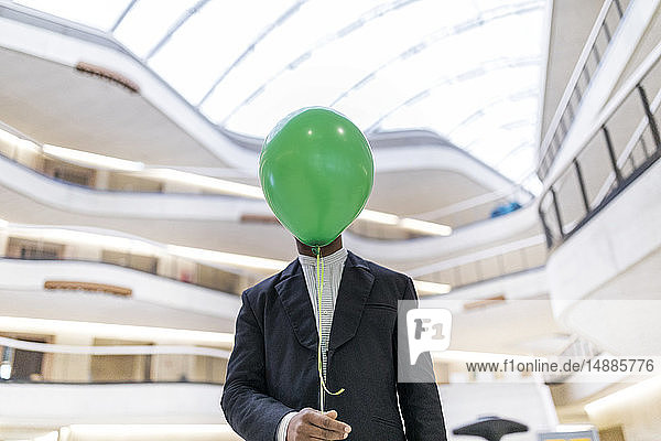 Reifer Geschäftsmann versteckt Gesicht hinter grünem Ballon