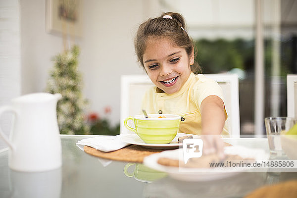 Glückliches kleines Mädchen nimmt beim Frühstück zu Hause einen Keks
