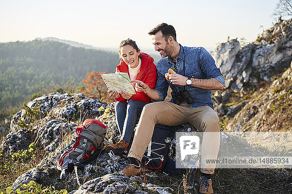 Happy couple on a hiking trip in the mountains taking a break looking at map
