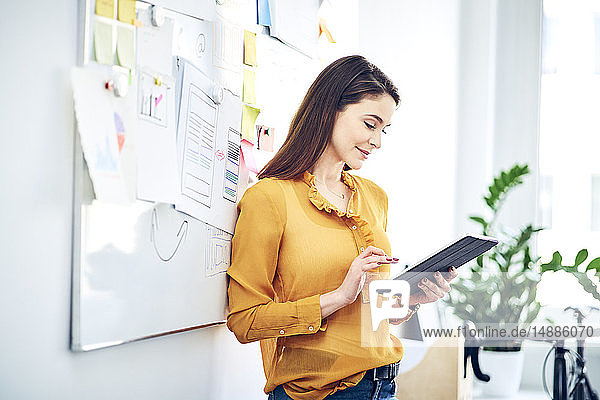 Lächelnde Geschäftsfrau benutzt Tablett am Whiteboard im Büro