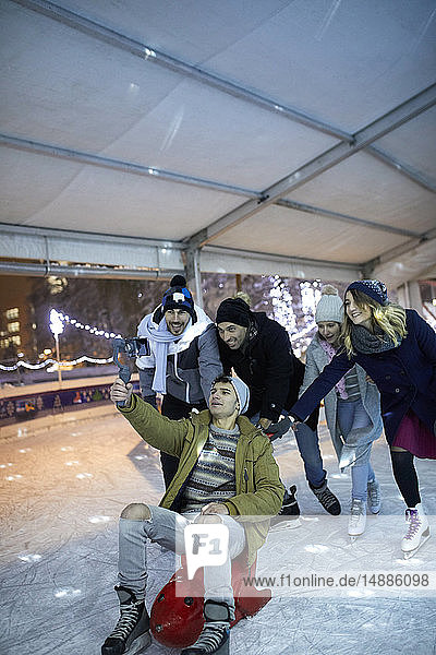 Glückliche verspielte Freunde mit einer Kamera beim Schlittschuhlaufen auf einer Eisbahn