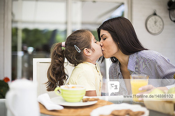 Mutter und Tochter küssen sich beim Frühstück zu Hause