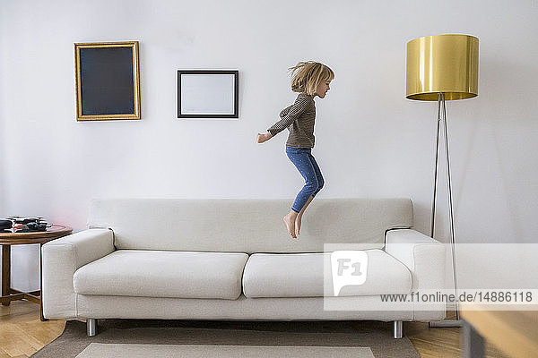 Kleines Mädchen  das zu Hause auf der Couch in die Luft springt