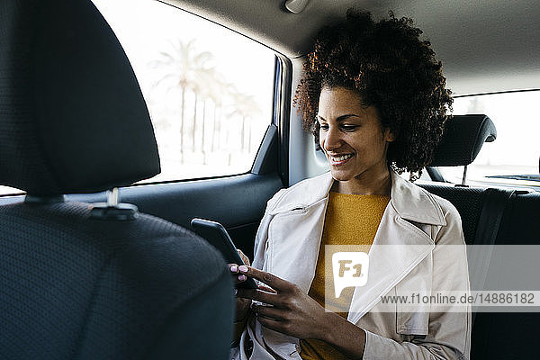 Lächelnde Frau sitzt auf dem Rücksitz eines Autos und benutzt ein Mobiltelefon