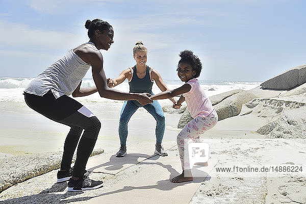 Mutter mit Tochter und Freundin bei einer Fitnessübung am Strand