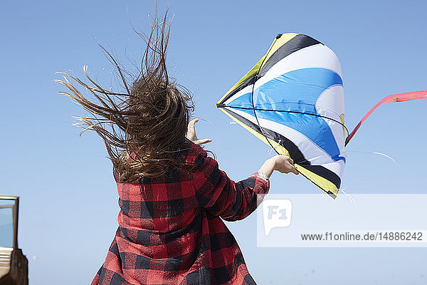 Mädchen mit windgepeitschtem Haar fliegt Drachen unter blauem Himmel