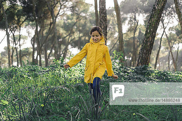 Smiling girl wearing yellow raincoat and walking in the woods