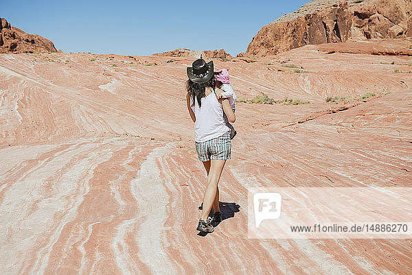 USA  Nevada  Valley of Fire State Park  Rückenansicht einer Mutter mit Mädchen auf dem Arm in rötlicher Landschaft