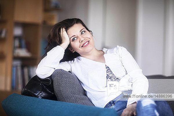 Porträt einer lächelnden jungen Frau  die zu Hause auf einer Couch sitzt und sich entspannt
