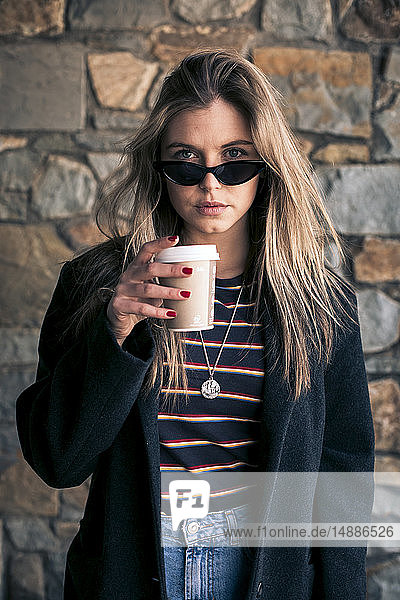 Porträt einer jungen Frau mit Sonnenbrille und Kaffee zum Mitnehmen