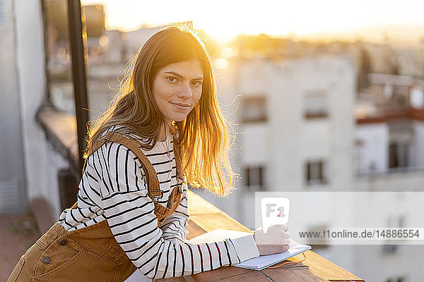 Porträt einer jungen Frau  die bei Sonnenuntergang auf der Dachterrasse Notizen macht