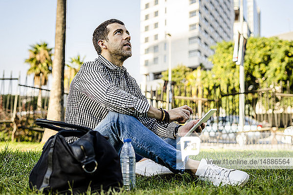 Mann sitzt auf einer Wiese im Stadtpark und schaut mit einem digitalen Tablet auf