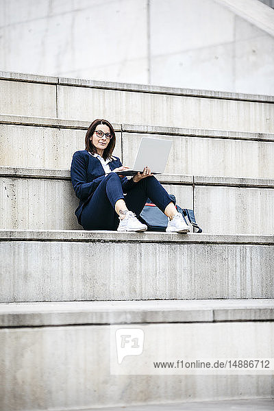 Porträt einer Geschäftsfrau  die mit einem Laptop im Freien auf einer Treppe sitzt