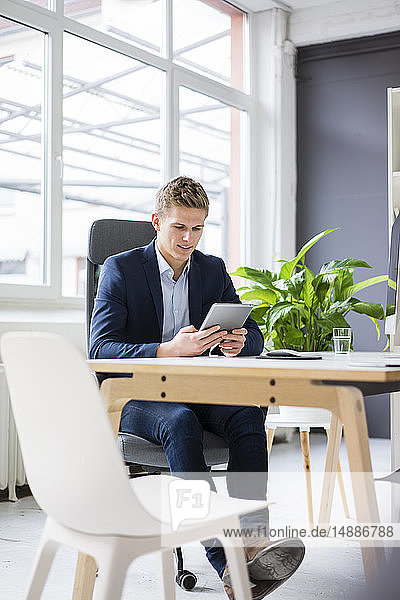 Selbstbewusster junger Geschäftsmann sitzt am Schreibtisch im Büro mit Tablett