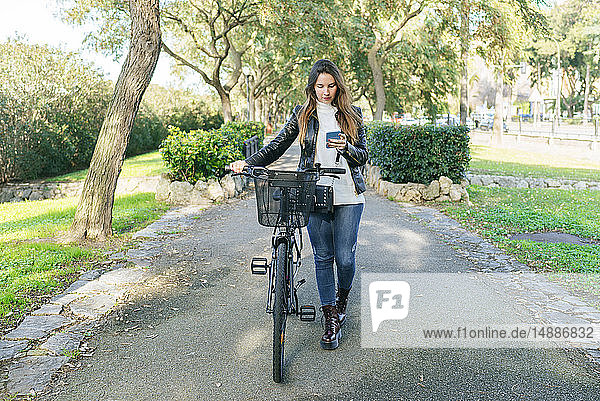 Junge Frau mit Fahrrad im Park mit Mobiltelefon
