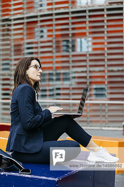 Geschäftsfrau sitzt mit Laptop vor einem Bürogebäude in der Stadt