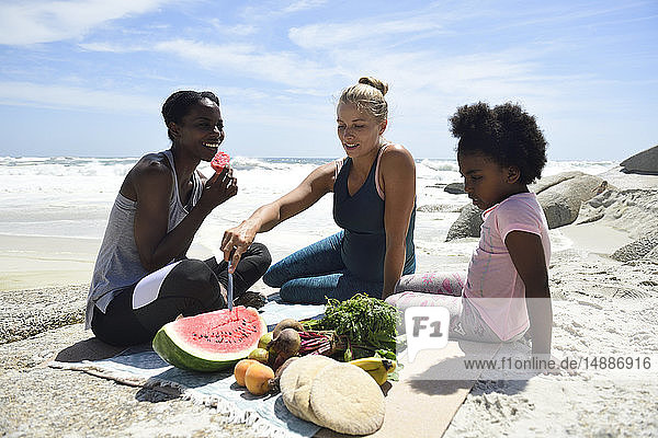 Mutter mit Tochter und Freundin beim Picknick am Strand
