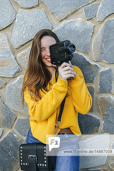 Junge Frau mit Oldtimer-Kamera an einer Steinmauer