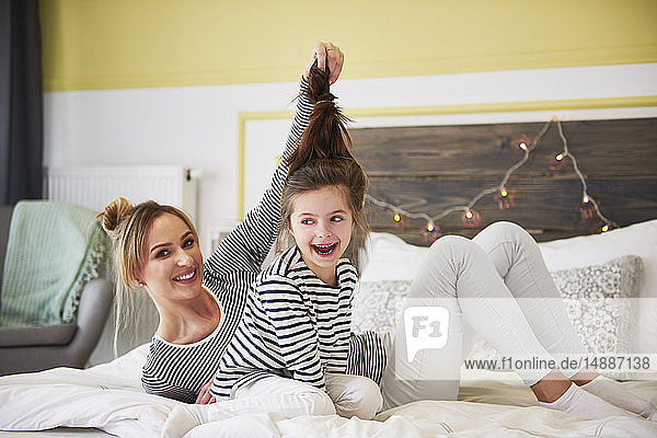 Mother and daighter sitting on bed  mother holding daughter's ponytail
