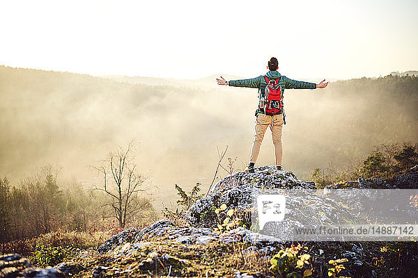 Mann auf einer Wanderung in den Bergen steht auf einem Felsen und genießt die Aussicht