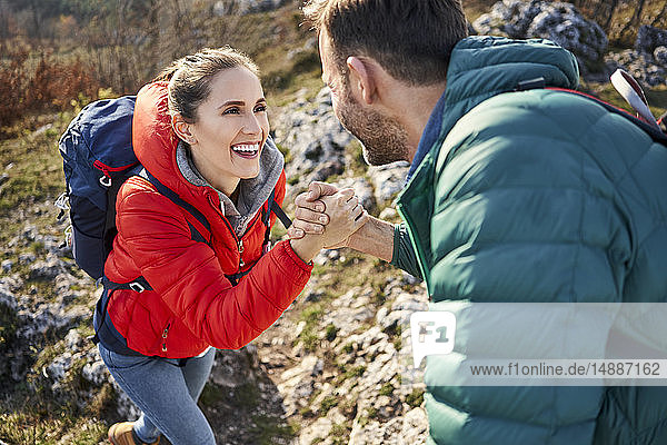 Man helping girlfriend climbing rock on a hiking trip in the mountains
