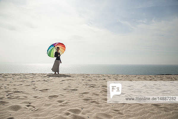 Frau mit buntem Regenschirm am Strand spazieren