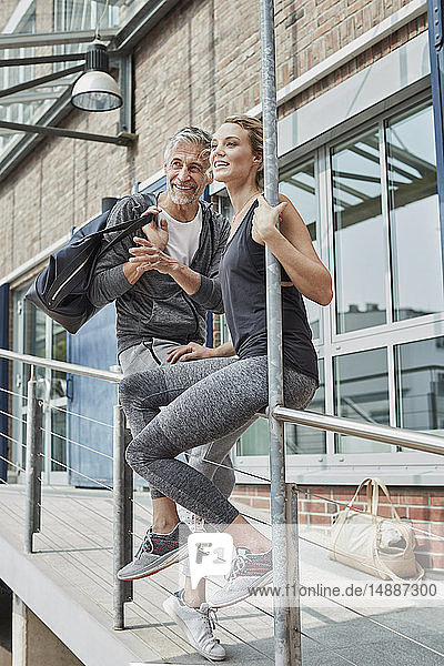 Porträt eines reifen Mannes mit Sporttasche und einer jungen Frau vor einer Sporthalle  die etwas beobachtet
