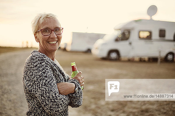 Porträt einer lächelnden Frau mit Bierflasche auf dem Campingplatz am Abend