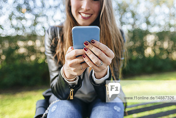 Nahaufnahme einer jungen Frau  die auf einer Parkbank sitzt und ein Mobiltelefon benutzt