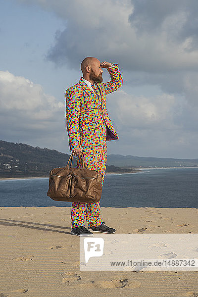 Spain  Tarifa  man with travelling bag wearing suit with colourful polka-dots standing on dune looking at distance