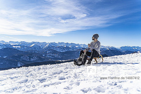 Deutschland  Bayern  Brauneck  Mann im Winter in den Bergen bei einer Pause