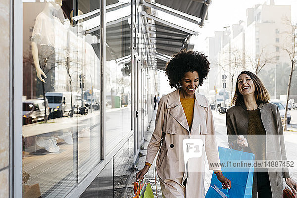 Zwei glückliche Frauen mit Einkaufstaschen gehen in der Stadt spazieren