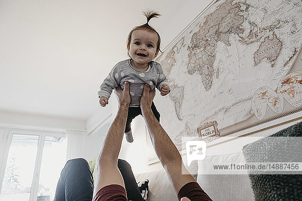 Glückliches Mädchen wird zu Hause im Wohnzimmer von ihrem Vater hochgehoben