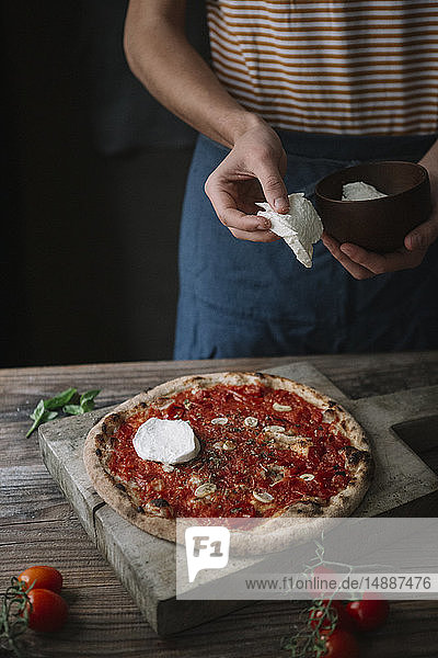 Junger Mann bereitet Pizza zu  hält Mozzarella in der Hand