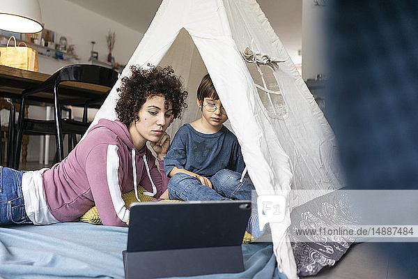 Mother and son lying in play tent  watching movie on tablet
