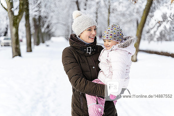 Glückliche Mutter trägt Tochter in Winterlandschaft