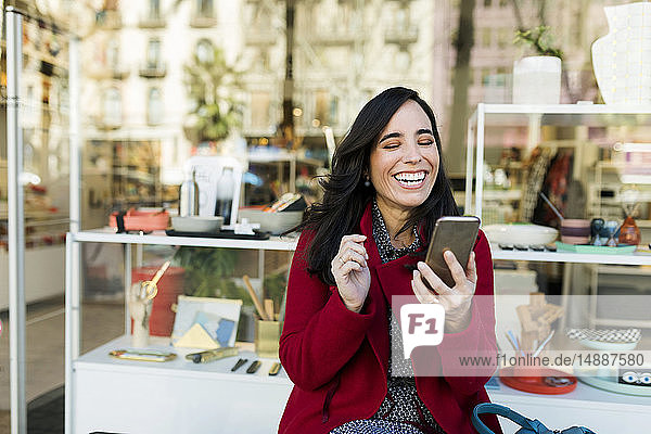 Glückliche Frau benutzt Handy vor dem Schaufenster
