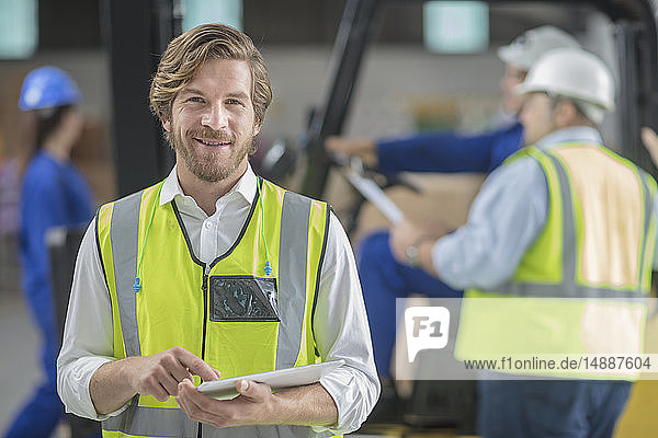 Porträt eines lächelnden Mannes mit reflektierender Weste mit Tablette in der Fabrik