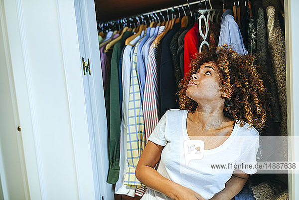 Junge Frau mit lockigem Haar zu Hause betrachtet Kleidung in ihrem Kleiderschrank