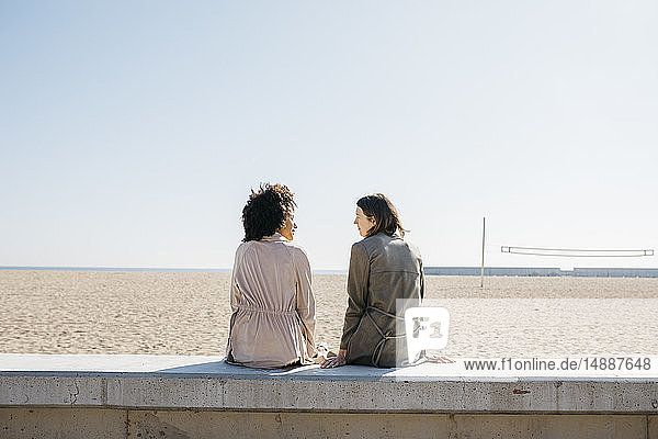 Back view of two friends sitting on the promenade enjoying leisure time