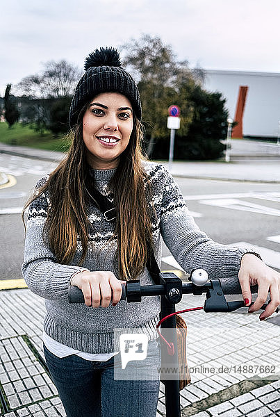 Porträt einer lächelnden jungen Frau mit Elektroroller in der Stadt
