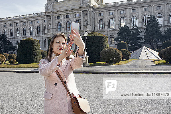 Österreich  Wien  Porträt einer lächelnden jungen Frau  die mit dem Smartphone Selbsthilfe nimmt