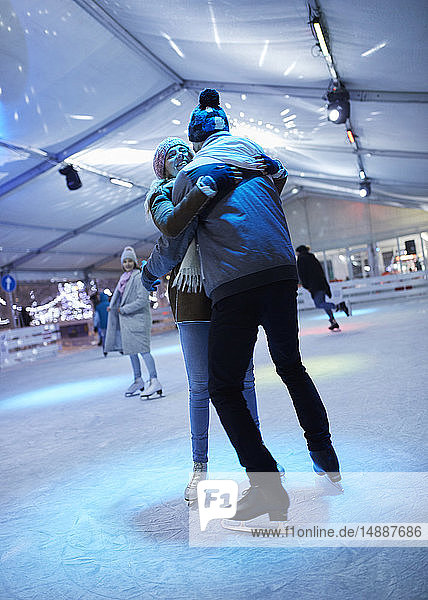Glückliches junges Paar umarmt sich nachts auf einer Eisbahn