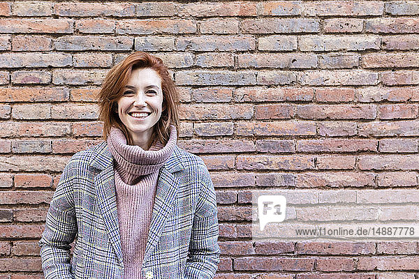 Porträt einer glücklichen jungen Frau  die an einer Ziegelmauer steht