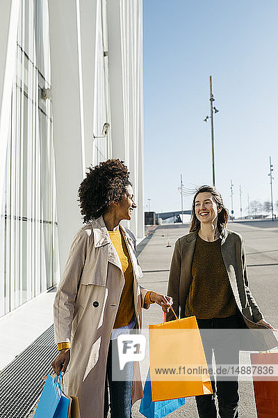 Zwei glückliche Frauen mit Einkaufstaschen gehen in der Stadt spazieren