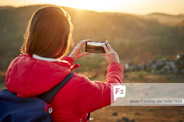Frau auf einer Wanderung  die bei Sonnenuntergang ein Smartphone-Foto macht