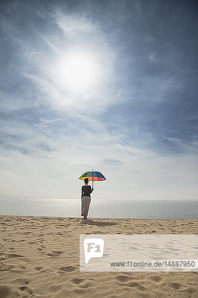 Woman with colorful umbrella standing at the beach  rear view