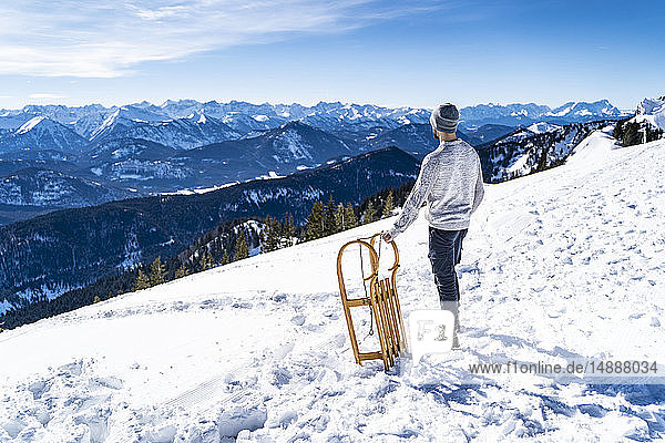 Deutschland  Bayern  Brauneck  Mann mit Schlitten im Winter in den Bergen beim Anblick